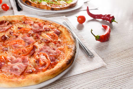 Pizza with chicken, mushrooms, cheese, sauce, ham, salami, pepper chili, tomatoes on a dark wooden table.の写真素材