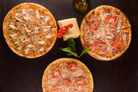Pizza with chicken, mushrooms, cheese, sauce, ham, salami, pepper, tomatoes on a dark wooden table....