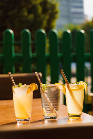 Cocktails with lemon and mint in glasses with tube on a wooden table against the background of a restaurant. Cold lemonadeの写真素材
