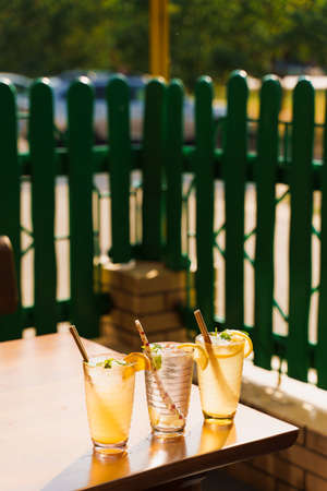 Cocktails with lemon and mint in glasses with tube on a wooden table against the background of a restaurant. Cold lemonadeの写真素材