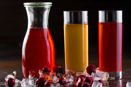 Compote berry, fruit in a jar and glasses on a dark wooden table. Summer lemonade. Decorated with ice and cherries, raspberries.の写真素材