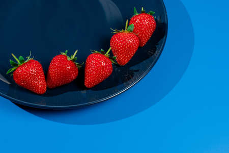 Bunch of strawberry on plate on blue background. Summer seasonal red berry