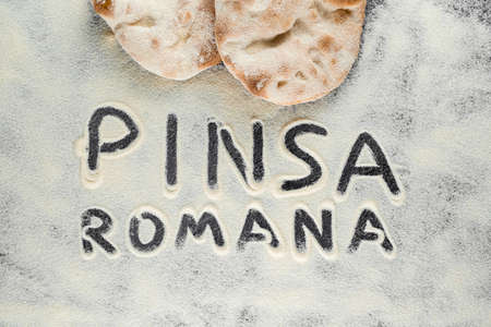 Dough and flour with text pinsa romana on black background. Scrocchiarella gourmet italian cuisine. Traditional dish in italyの写真素材