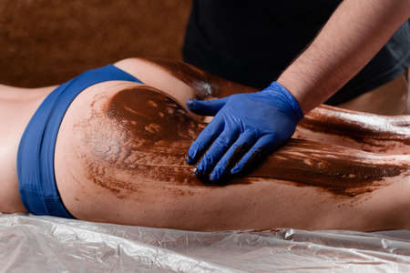 The masseur smears chocolate on the legs and thighs of the girl in the spa center. Beauty procedure chocolate wrapの写真素材