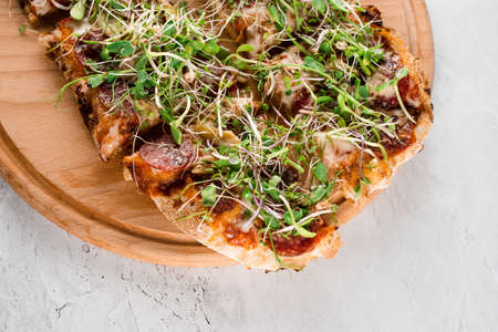 Pinsa romana with salami, cheese, mushrooms, decorated with microgreens on wooden boardon white backgroundの写真素材