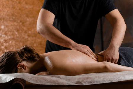 Attractive girl is relaxing on classic massage procedure in spa. Manual therapy. Masseur is doing back massageの写真素材