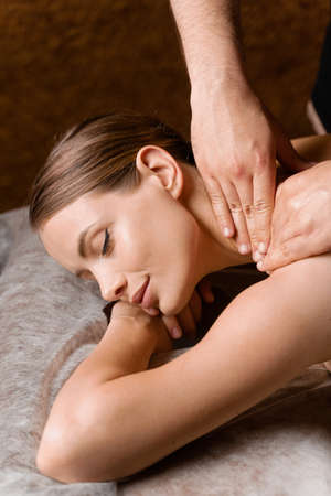 Attractive girl is relaxing on classic massage procedure in spa. Manual therapy. Masseur is doing shoulder massageの写真素材