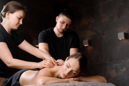 4 hands massage in spa. Two masseurs are making four hands relaxing massage with oil for girl. Relaxation. Manual therapy.の写真素材