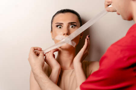 Model with glued mouth. Man covers woman mouth with tape. Stop talkingの写真素材