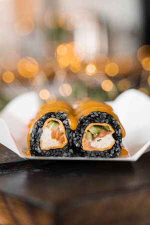 Sushi black roll on the new year lights background. Christmas lights decoration. Food delivery at new year eve. Roll with black rice, salmon, cucumber and cheeseの写真素材