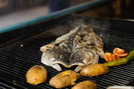 Cooking sea bass and vegetables. Grilling fish with chili potatoes and tomato