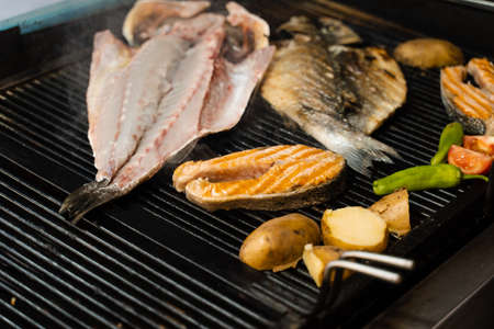 Cooking seafood mix of salmon, sea bass and vegetables. Grilling fish with chili potatoes and tomato