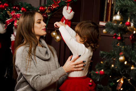 Mom and daughter decorate the christmas tree before the new year. Family traditions. Preparing for new year celebrationの写真素材