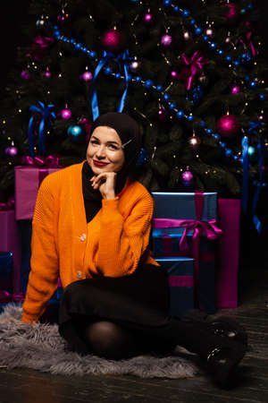 Muslim girl in black hijab is dreaming about gift at new year holiday. Christmas celebration of...
