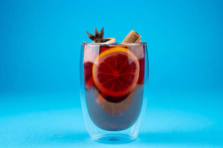 Mulled wine on blue background. Alcohol punch in double glass cup. Drink with orange, anise star, cinnamon and appleの写真素材