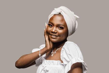 Beauty portrait of black muslim woman weared white dress and headscarf on gray background. Softness and wellness of body and skinの写真素材