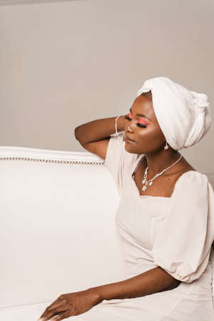 Black muslim business woman is sitting on the sofa. Confident lady weared white dress and headscarfの写真素材
