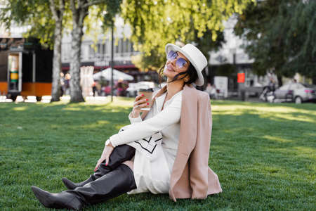 Business lady with cup of coffee on the grass. Model weared official style is sitting on the grass, smiling and posingの写真素材