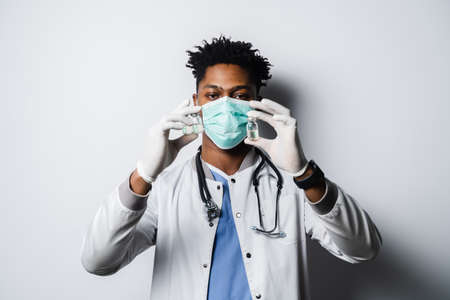 Handsome African doctor with coronavirus covid-19 vaccine. Black doctor in medical mask is holding vaccine on white backgroundの写真素材