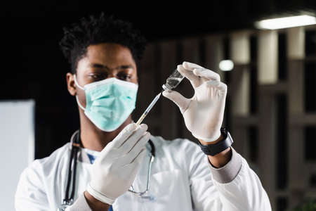African doctor in a medical mask prepares to inject coronavirus covid-19 vaccine. Black doctor in...