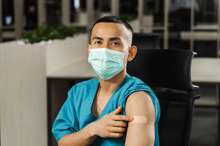 Handsome asian man vaccinated against coronavarus and showing patch on his arm. Covid-19...