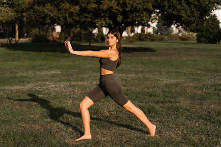Qigong meditation exercises outdoor. Fit asian girl does chinese training on the green grass in the...