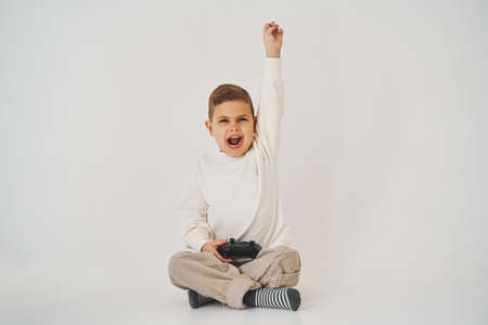 Emotional child with a gamepad rejoices, shouts and raises his hands up because he won the gameの写真素材