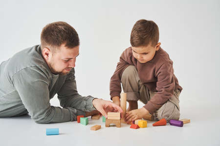 Caring dad plays with cheerful son with toy wooden cubes on white background. Fatherhood and child careの写真素材