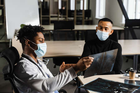 Asian patient at African doctor appointment. Fracture of the bones of foot. Black surgeon showing x-ray to patientの写真素材