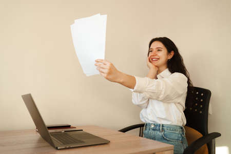 Applicant with laptop holds papers with exam results in his hands and rejoices. Student girl passed exam and rejoices at high mark. Online education and distance learningの写真素材
