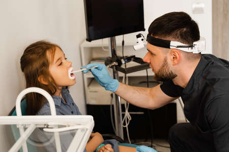 Oropharyngoscopy procedure. Otolaryngologist examines child throat with spatula. Consultation with...