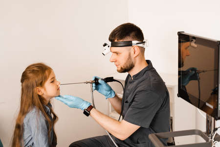 Nose endoscopy of child. Rhinoscopy procedure with rhinoscope. ENT doctor otolaryngologist with headlight treat nose kid patientの写真素材