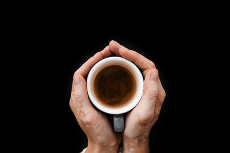 Hands with vitiligo skin pigmentation holding cup of coffee on black background close-up. Lifestyle...