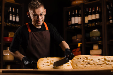 Cheese sommelier in food shop worker is cutting limited maasdam natural aged and check quality. Handsome bearded man working in food storeの写真素材