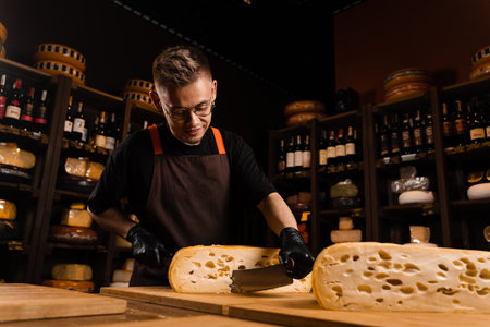 Cheese sommelier in food shop worker is cutting limited maasdam natural aged and check quality. Handsome bearded man working in food storeの写真素材