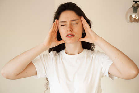 Depressed girl with migraine headache. Sad woman touches temples because of stress and despair in...