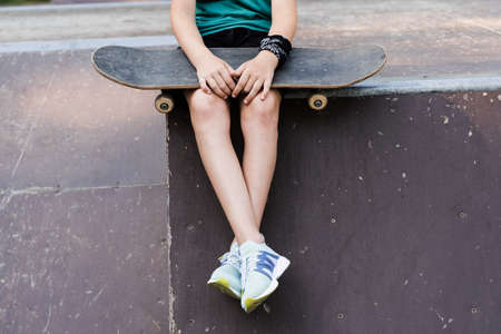 Child boy sitting with skate board close-up. Sports equipment for kids. Active teenager with on skate park playgroundの写真素材