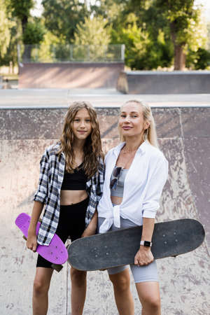 Mother and child daughter with skate and penny board training together in skate park. Extreme lifestyle. Family of mom and her kid spend time togetherの写真素材