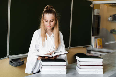 Education. Schoolgirl reading books and studying lesson at blackboard in school. Reading books....