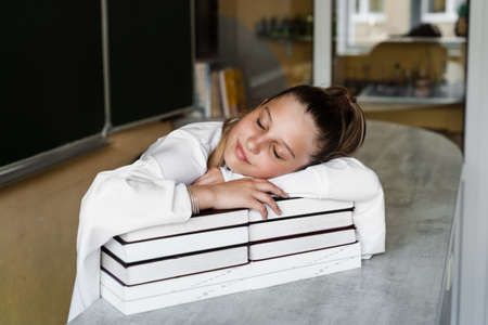 Tired schoolgirl lies and sleeping on books at blackboard in school. School education. The girl is...