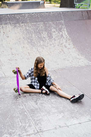 Active child girl after fall from penny board injured, sitting and looking at bruise on sport ramp on skate park playgroundの写真素材