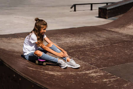 Active child girl after fall from penny board injured, sitting and feel pain on sport ramp on skate park playgroundの写真素材
