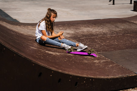 Active child girl after fall from penny board injured, sitting and feel pain on sport ramp on skate...