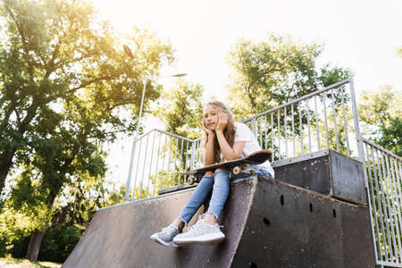Child girl sitting with skate board on sport ramp. Sports equipment for kids. Active teenager with skate board on skate park playgroundの写真素材
