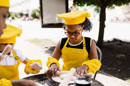Multiethnic cooks children in yellow chefs hat and apron cooking dough for bakery. Black african and...