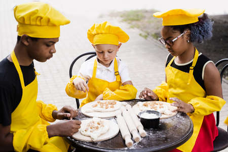 Happy company of multiethnic children cooking dough. Childhood cook activity of multinational children of black african and caucasian kidsの写真素材