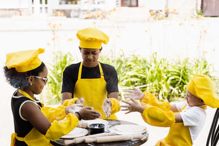 Multiracial children cooks play with flour for dough and having fun. Multinational cook kids in chefs hat and yellow apron uniform cooking outdoor for bakeryの写真素材