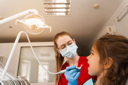 Child dentist makes professional teeth cleaning close-up in dentistry. Professional hygiene for teeth of child in dentistry. Pediatric dentist examines and consults kid patient in dentistryの写真素材