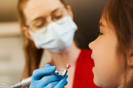 Child dentist makes professional teeth cleaning close-up in dentistry. Professional hygiene for teeth of child in dentistry. Pediatric dentist examines and consults kid patient in dentistryの写真素材