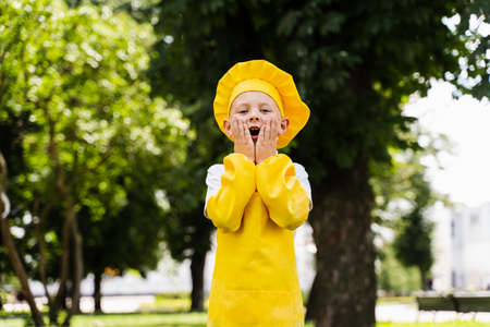 Shocked cook child in yellow chefs hat and apron yellow uniform holding his cheeks and surprise...